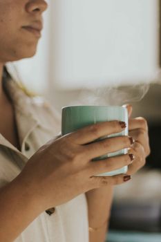 Close-up of a woman holding a steaming cup of coffee, creating a cozy atmosphere.
