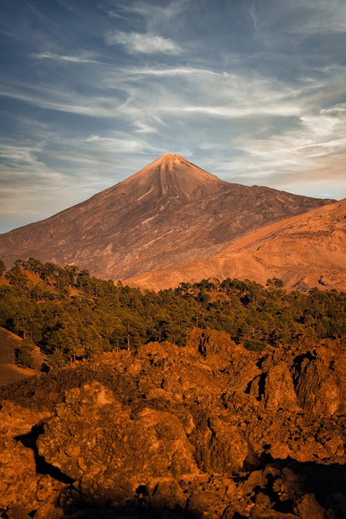 The sun sets over a mountain with rocks and trees