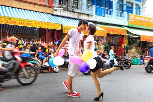 Man Kissing Woman While Holding Balloons