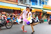 在熙熙攘攘的街道上，一对年轻夫妇手持五颜六色的气球，在热闹的市场上接吻