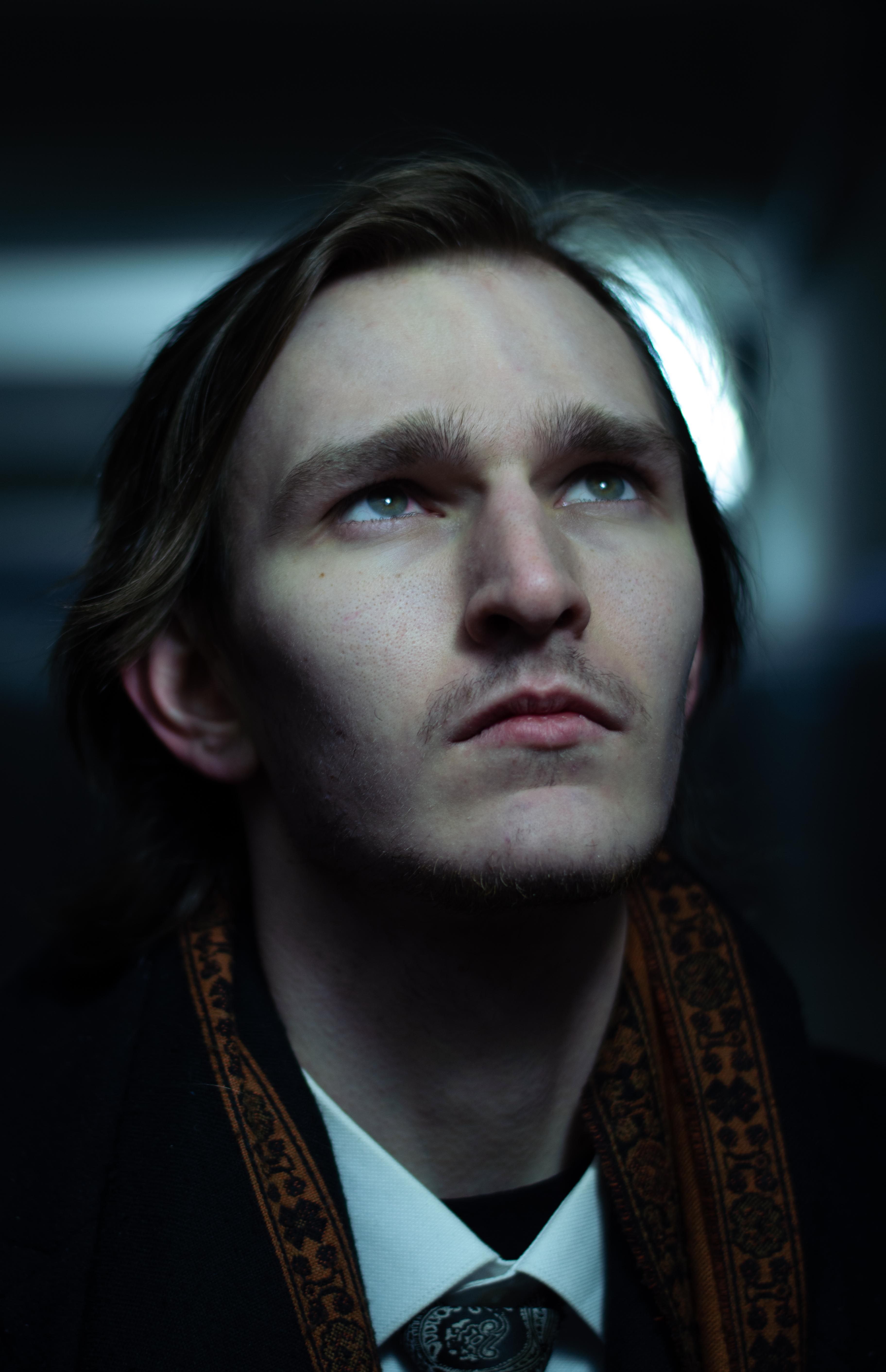 Portrait of a man with a mustache and beard gazing upwards in a dimly lit setting.