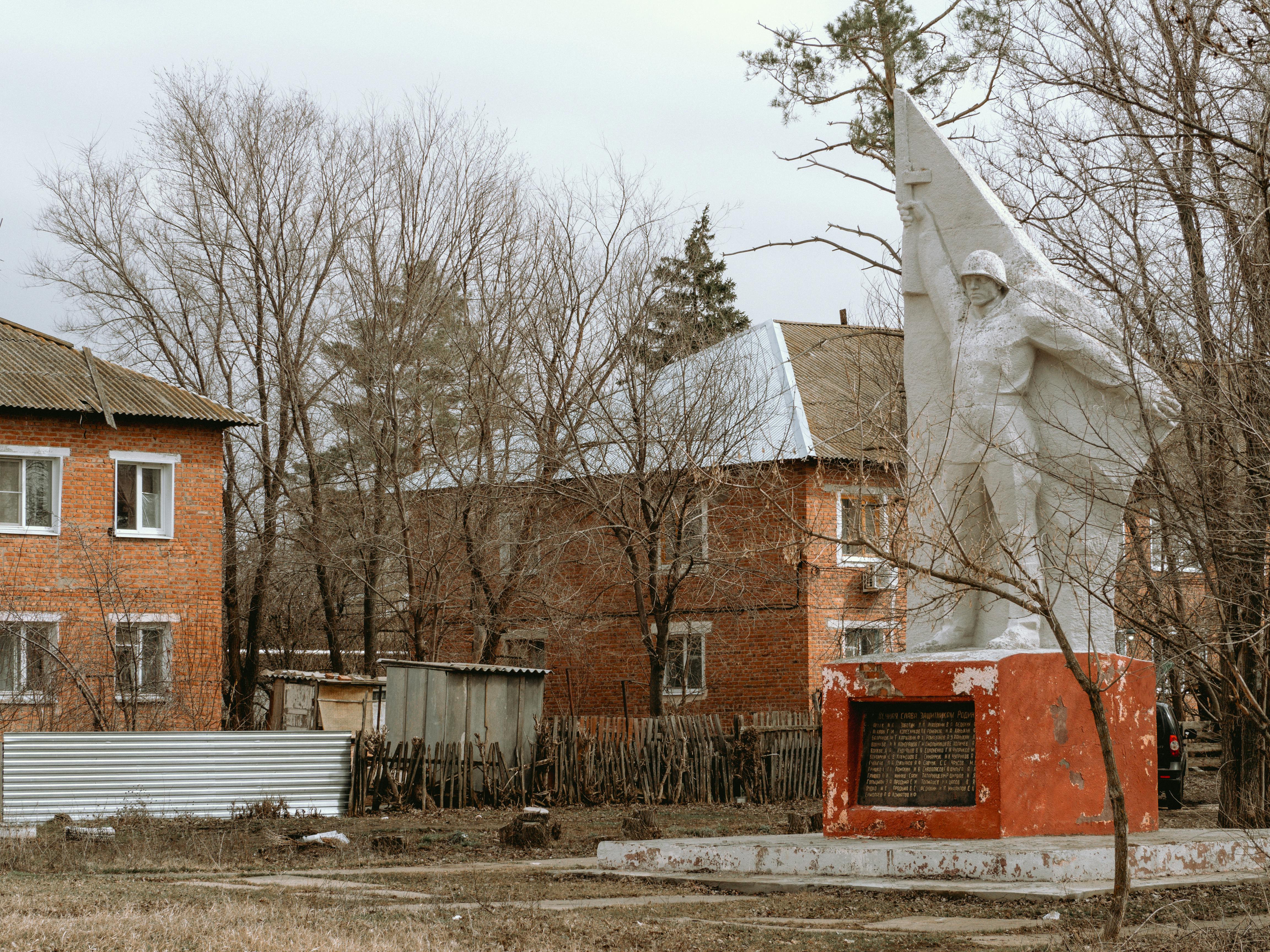 Statue of soldier in Семенной, Russia, surrounded by bare trees and houses.