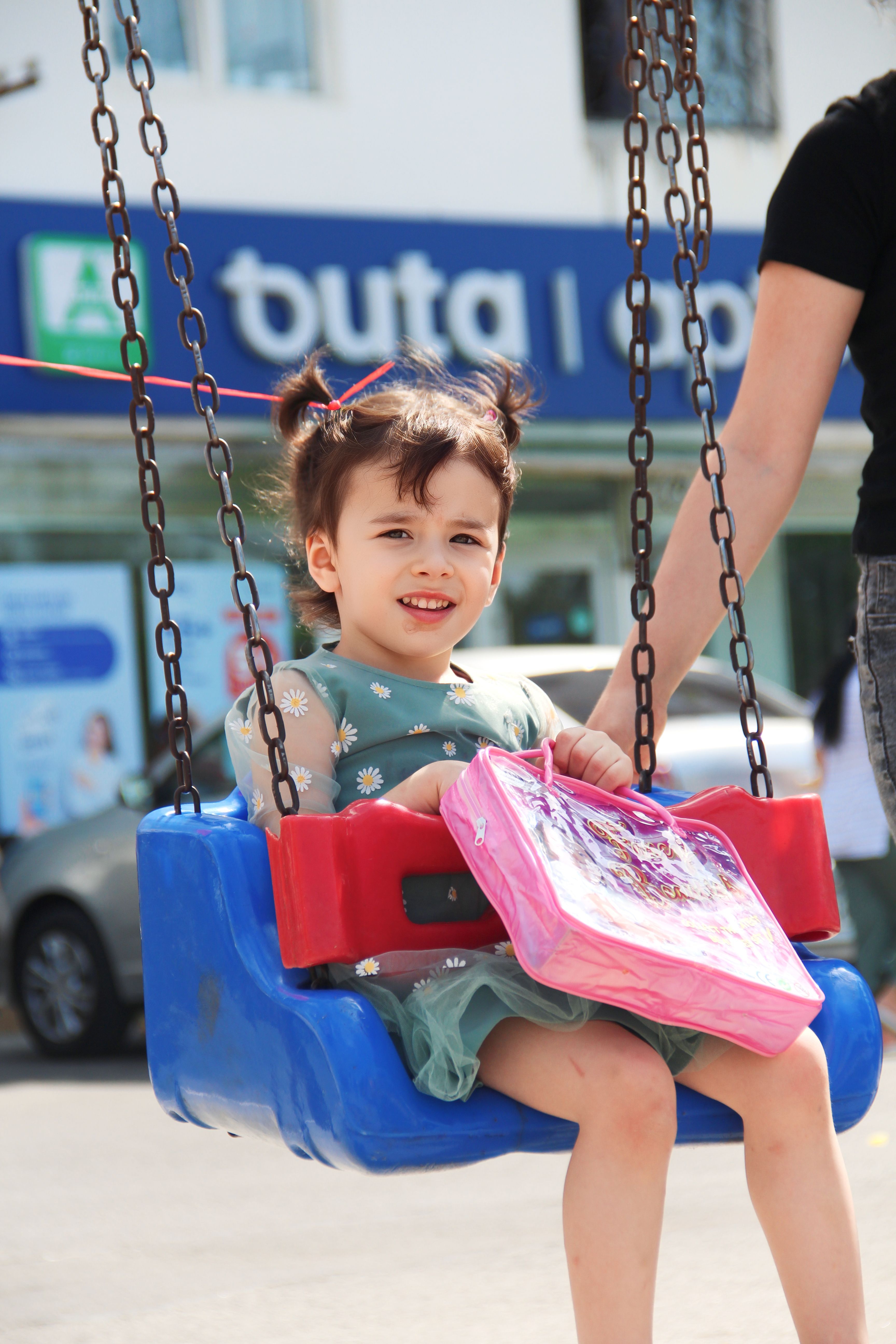 A young girl on a swing in an outdoor playground with supervision.