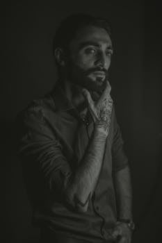 A dramatic monochrome portrait of a man with beard and tattoos, highlighting contemplation and depth.