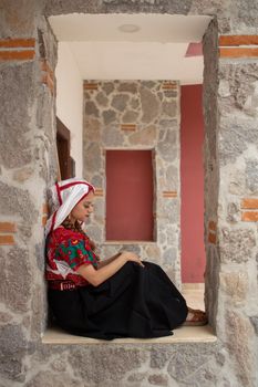 Woman in traditional attire sits by a stone wall, showcasing cultural fashion. — photo by Omar Tapia