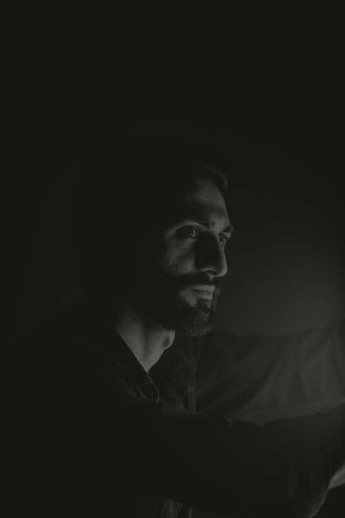 Free Black and white portrait of a man with a beard and mustache in low light, conveying a moody atmosphere. Stock Photo