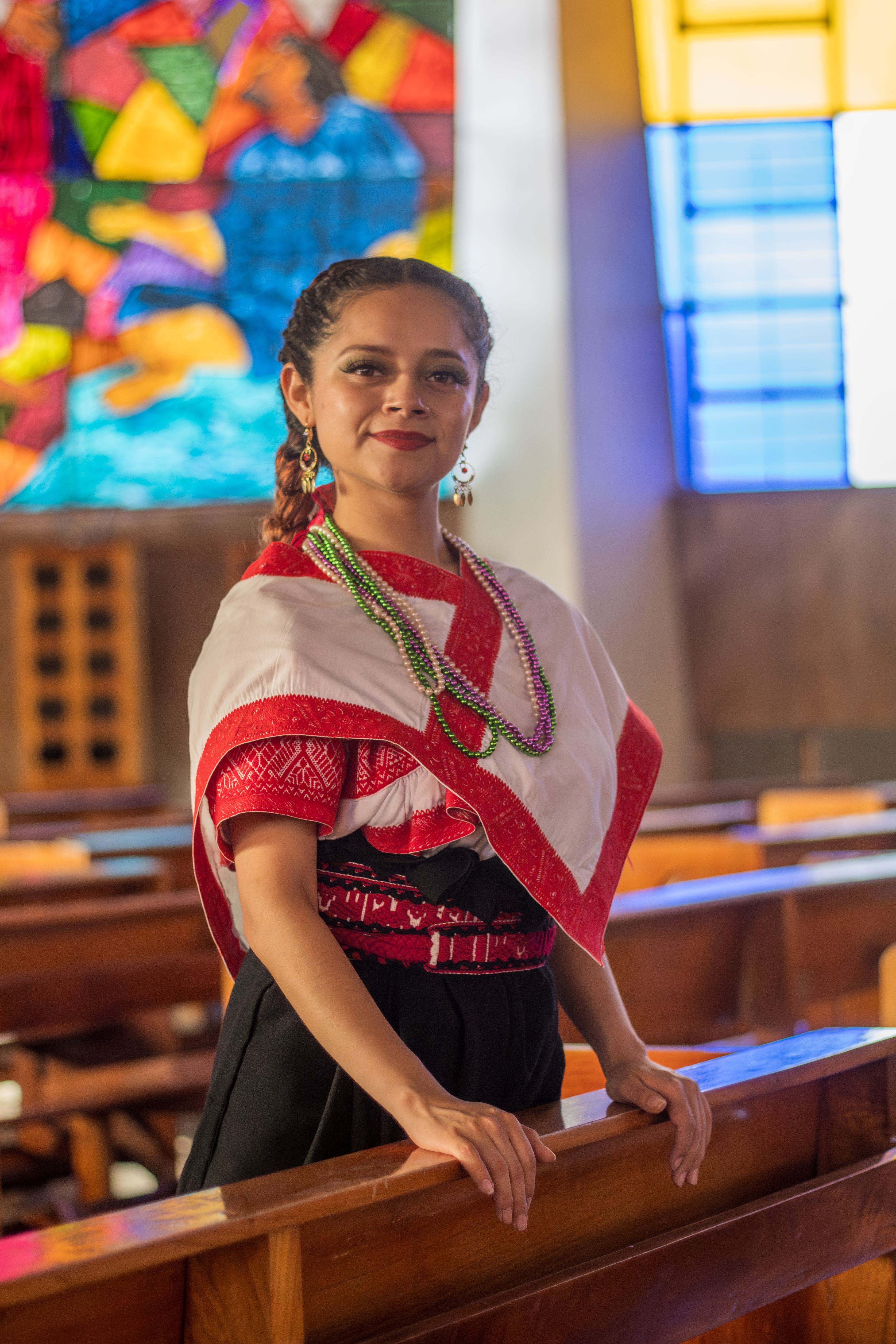 Woman in traditional attire inside a colorful church setting with stained glass.