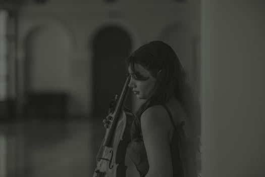 A serene black and white portrait of a female violinist standing indoors.