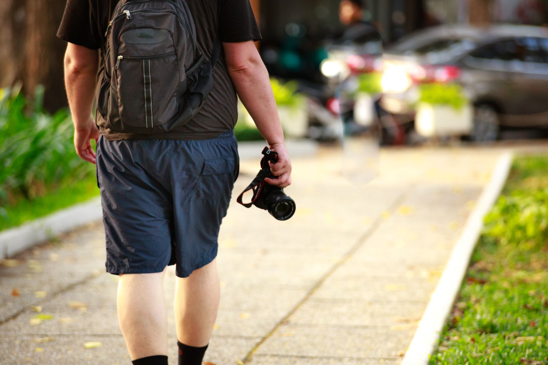 Man walking outdoors with a camera and backpack on a sunny day.