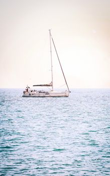 A solitary sailboat glides on calm blue ocean waters during a serene summer sunrise.
