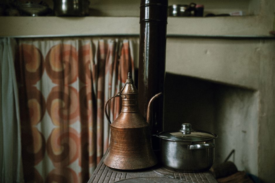 A copper kettle and stainless steel pot sit on a rustic stove in a cozy kitchen setting.
