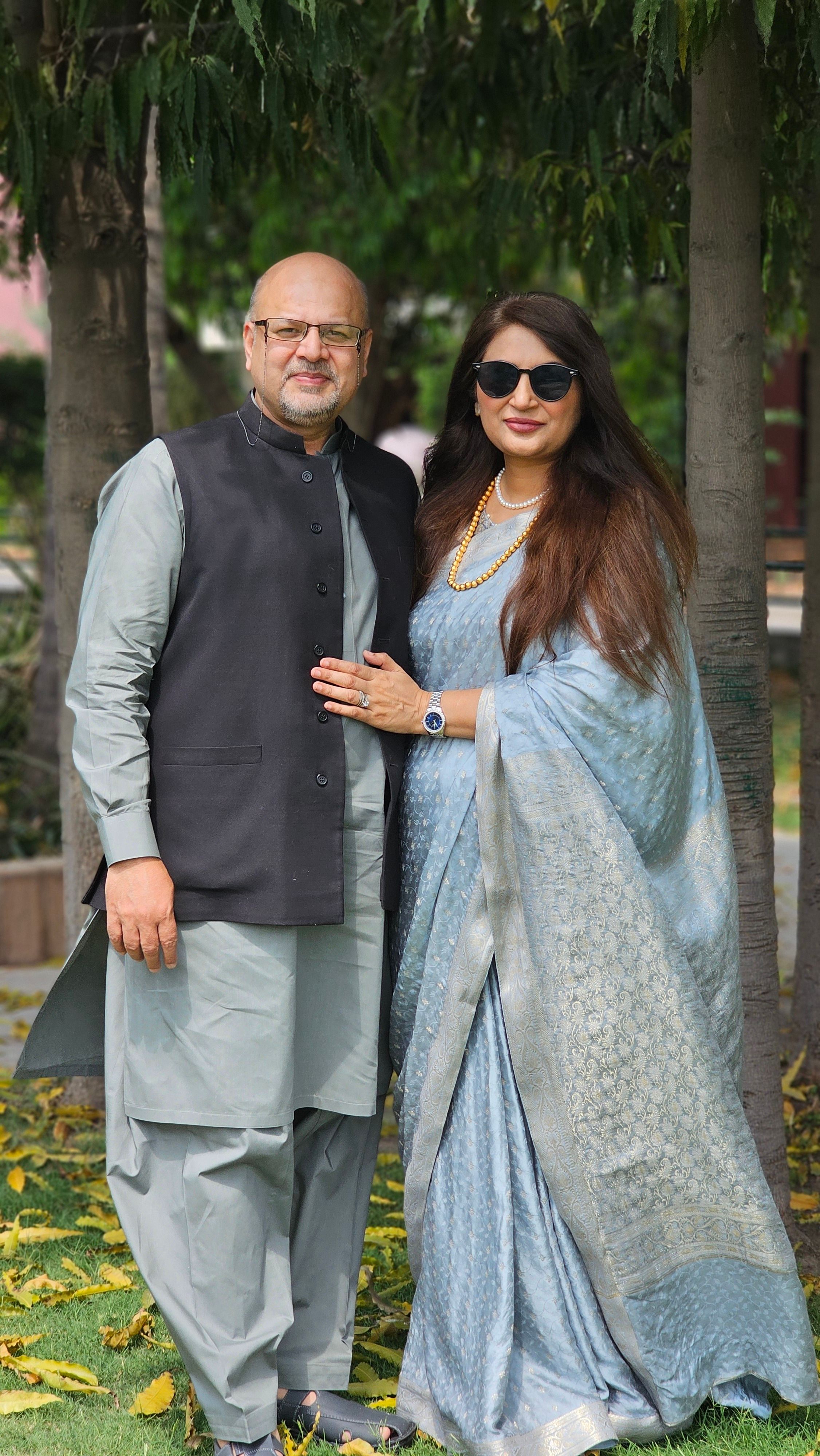 A couple standing together in traditional attire, embracing nature's beauty.