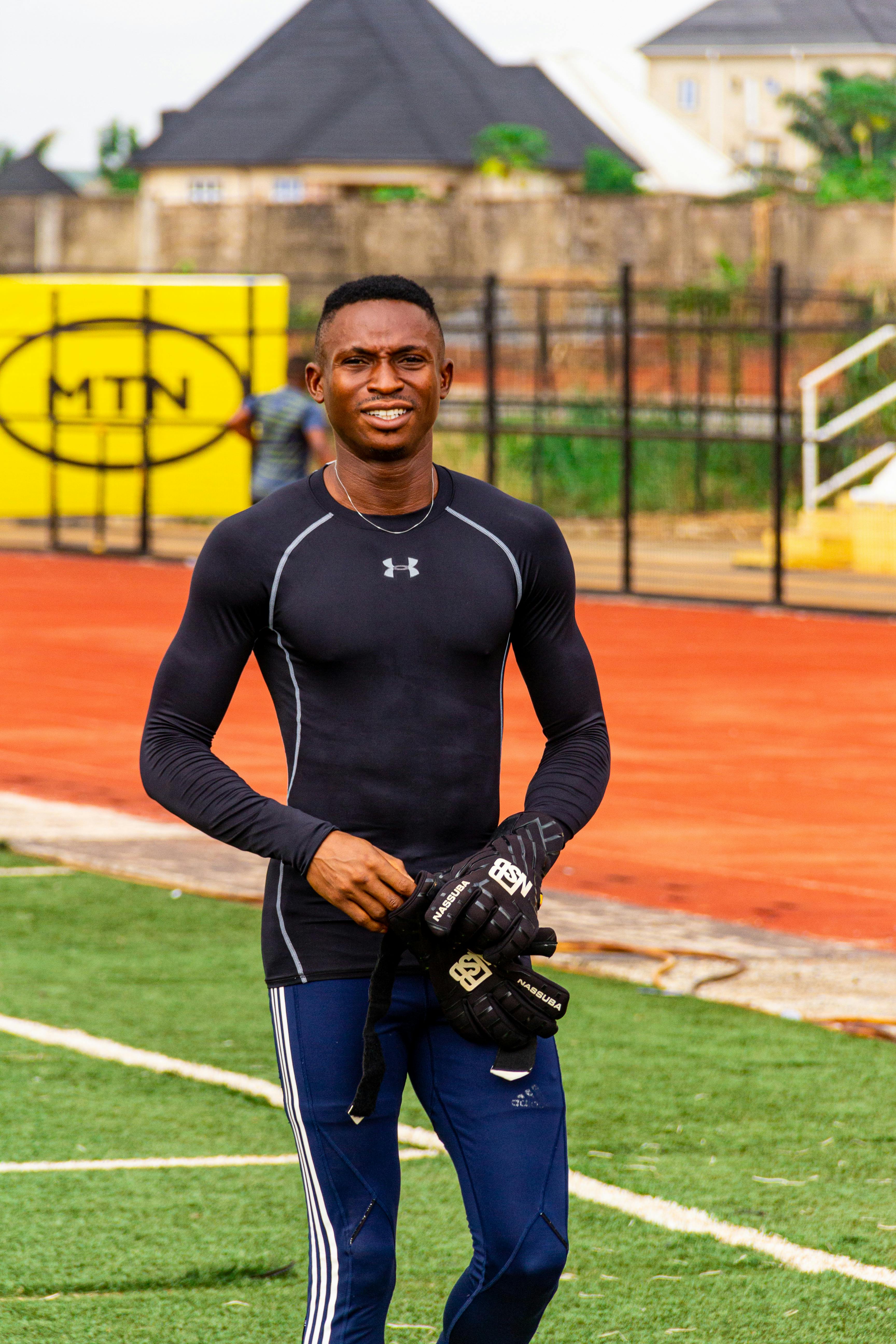 Portrait of a smiling male goalkeeper in sportswear holding gloves on an outdoor soccer field.