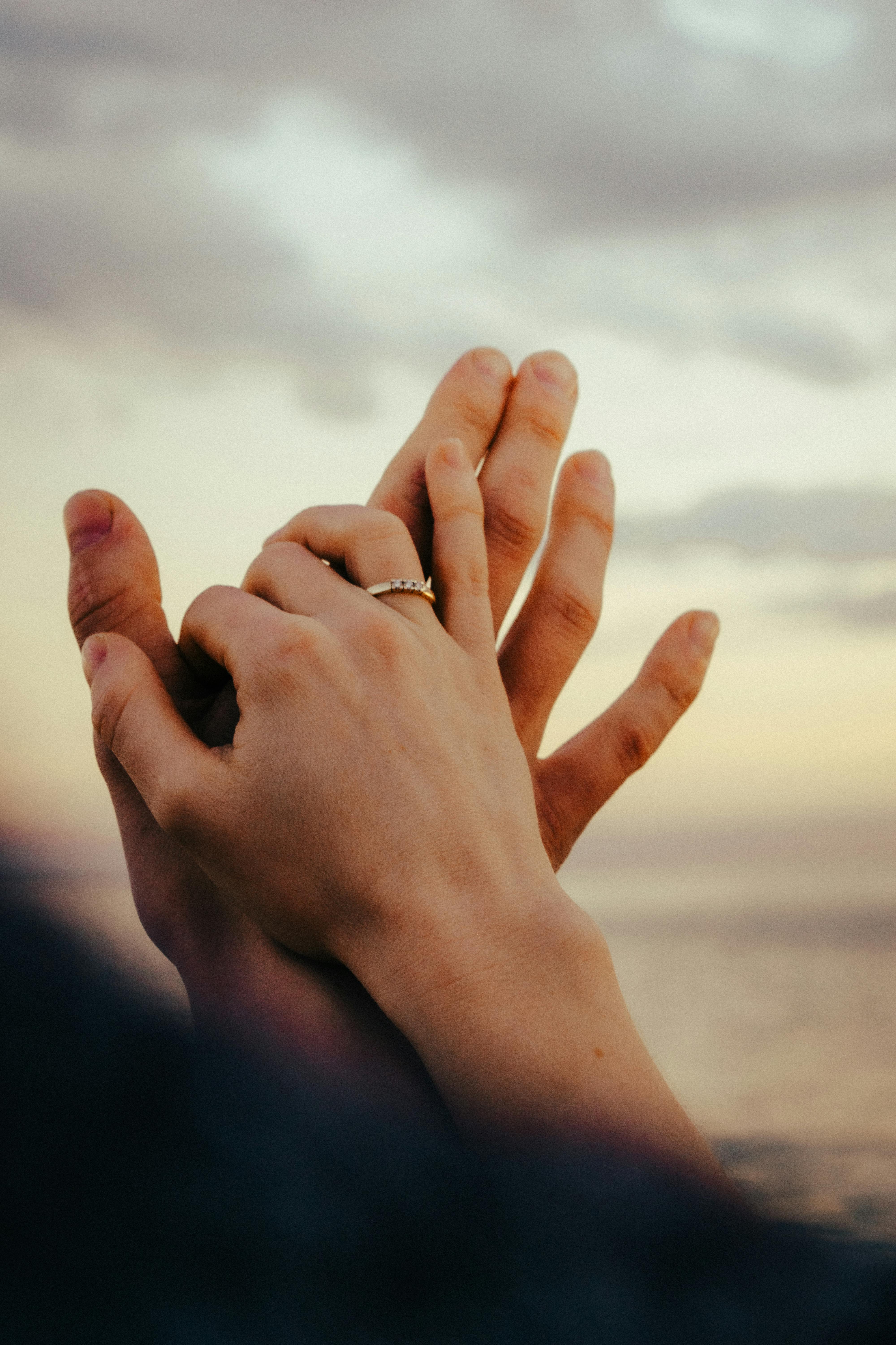 Free Close-up of a couple holding hands with a ring visible, set against a sunset sky. Stock Photo