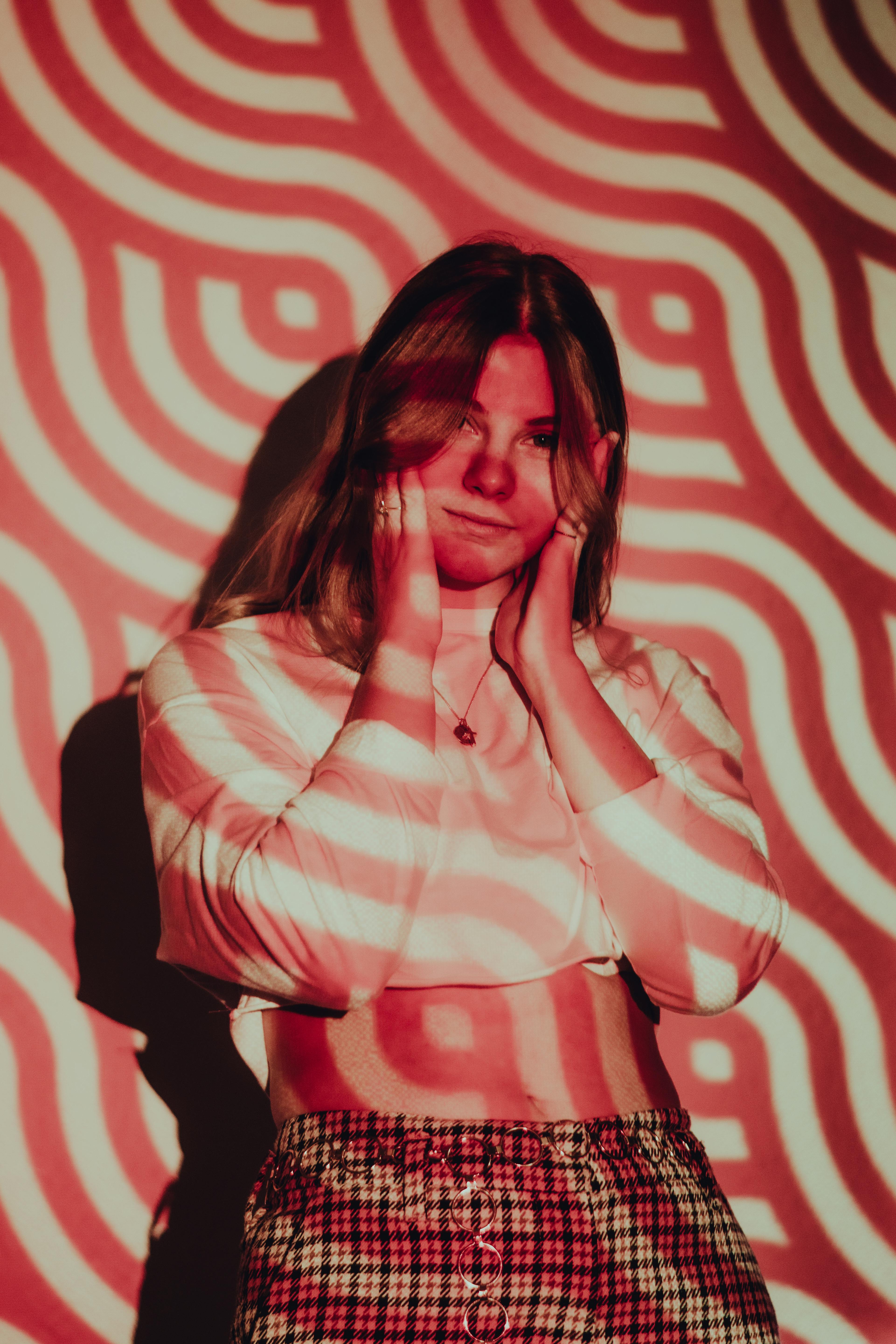 A woman poses creatively in studio with red psychedelic light patterns. Perfect for fashion and art themes.