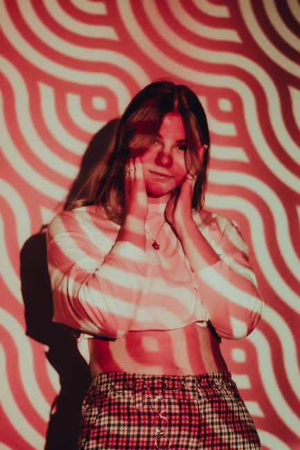 A woman poses creatively in studio with red psychedelic light patterns. Perfect for fashion and art themes.