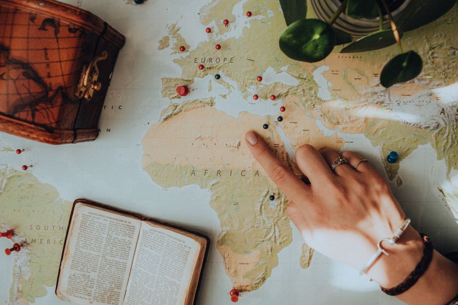 Hand pointing at a location on a world map — bufo ceremony costs $600–$1,500 CAD at ExploreBwiti Vancouver; Mexico-based providers typically run $1,000–$4,000 USD