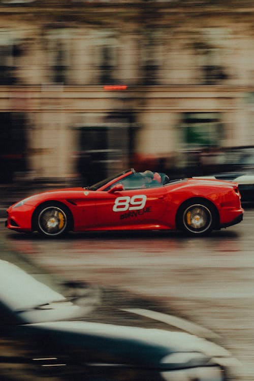 Free A red sports car driving down a street Stock Photo