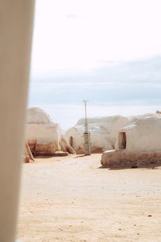 Sunlit desert village with traditional white adobe huts under a blue sky.