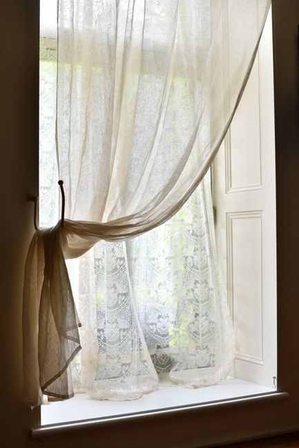 Soft lace curtains drape a sunlit window creating a cozy indoor atmosphere.