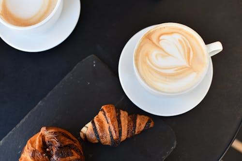 Two cups of coffee and croissants on a black table