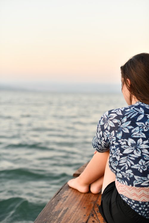 Free A woman sitting on a wooden boat looking out at the water Stock Photo