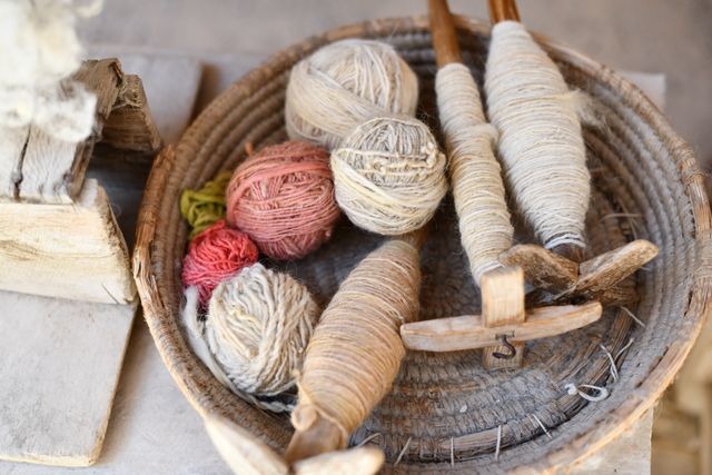 Hand-wound yarn balls and wooden spindles in a woven basket, photo by Rosa Stone on Pexels
