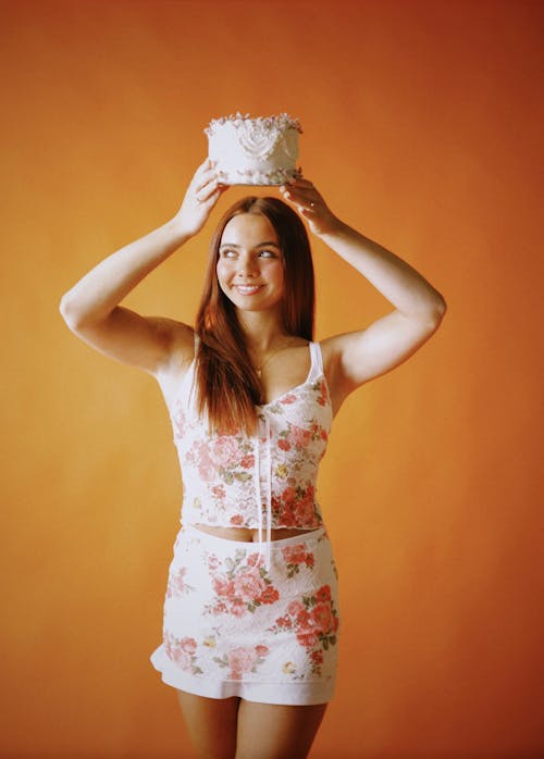 Smiling Woman Standing with Birthday Cake in Raised Arms
