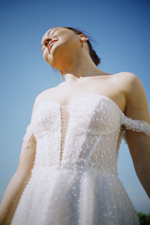 A woman in a wedding dress is looking up at the sky