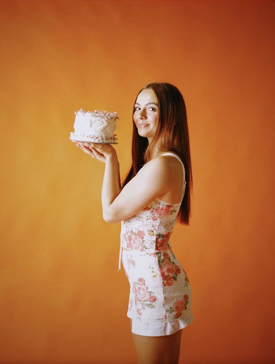 A woman holding a cake in front of an orange background