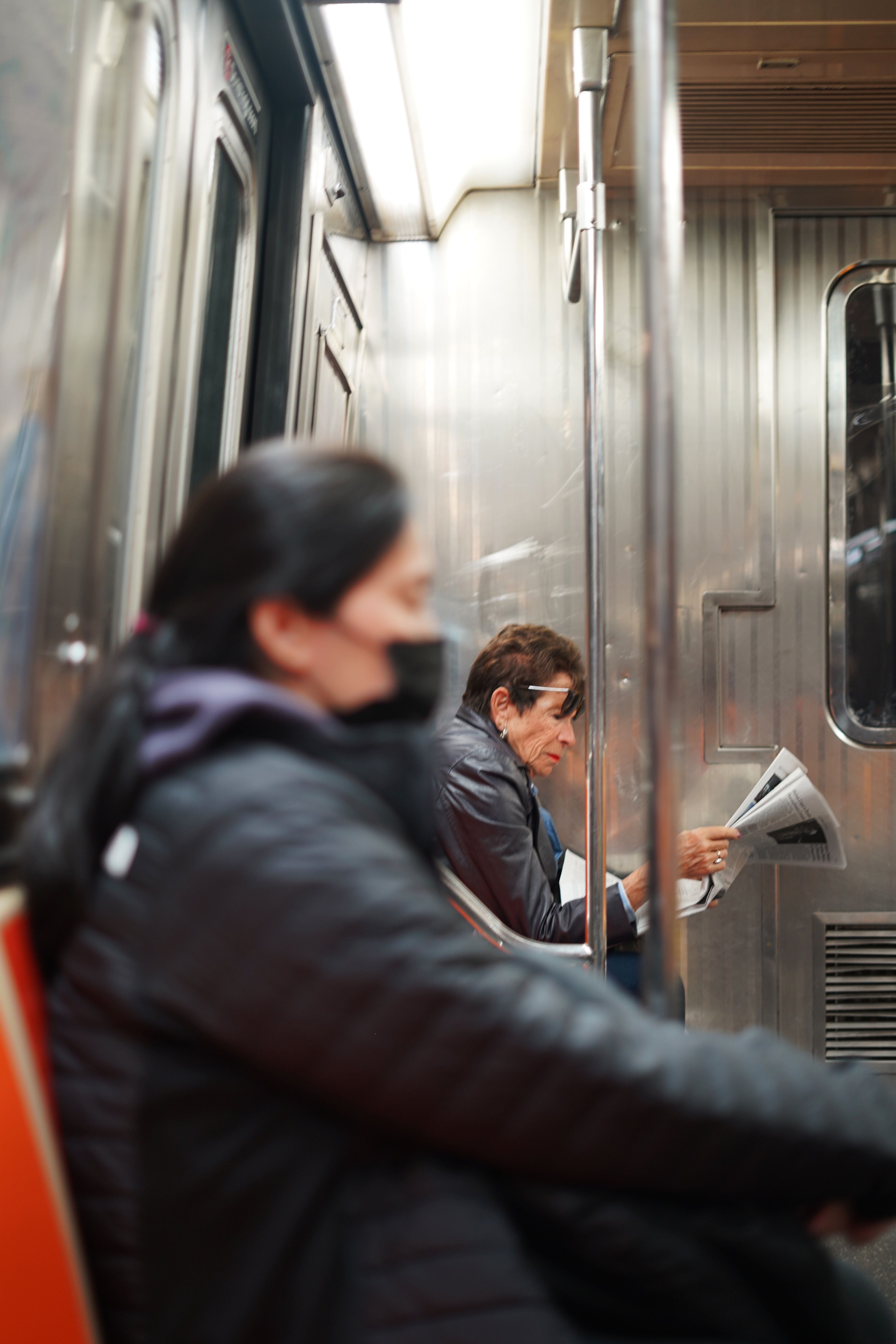 Two adults, one reading a newspaper, inside a bustling urban metro train.