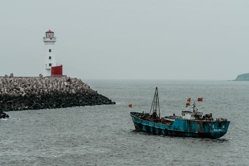 Free A serene coastal scene with a lighthouse and a fishing vessel in calm waters. Stock Photo
