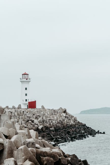 Serene lighthouse standing on a rugged coastline, guiding ships across a calm sea.