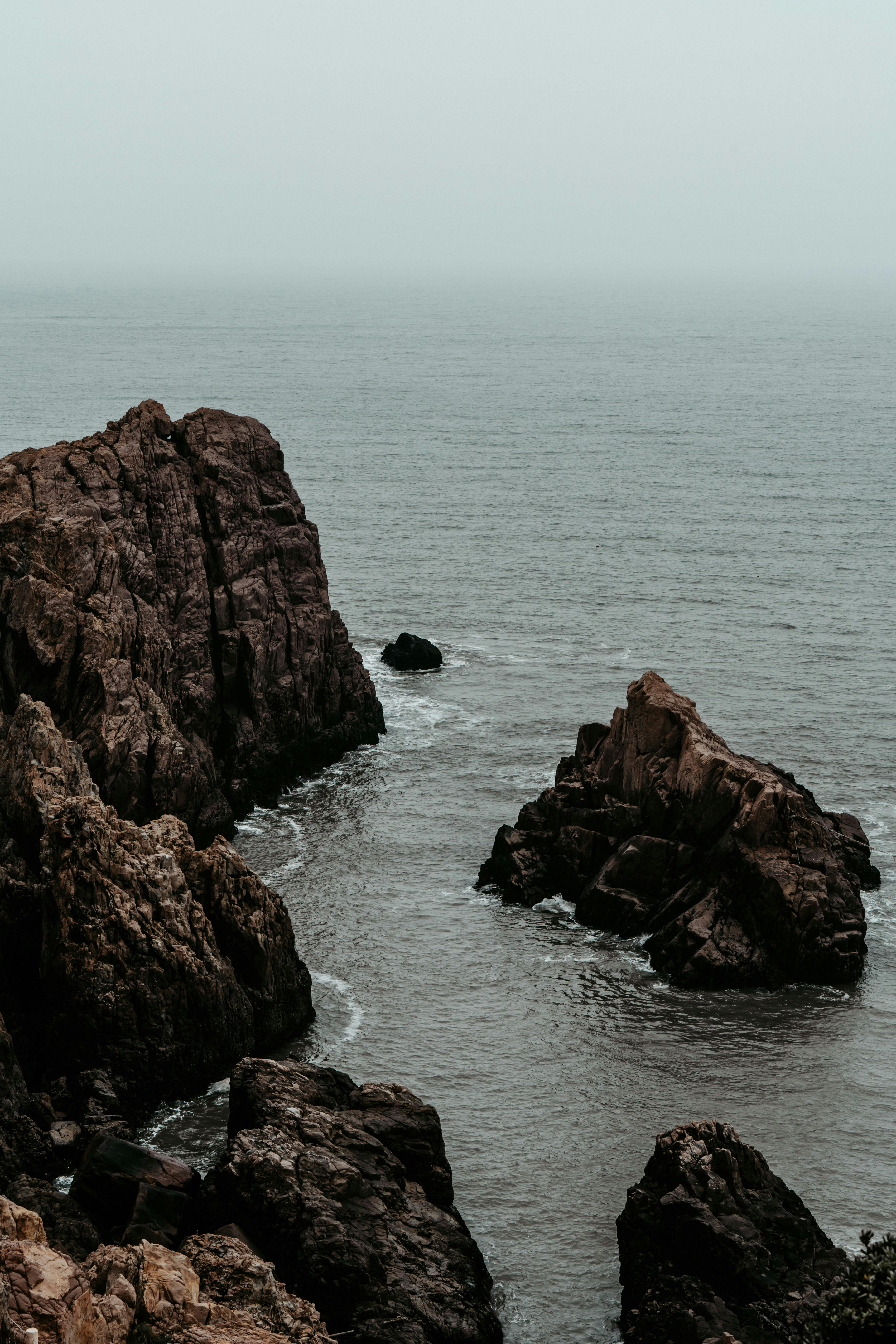 A stunning rocky coastline with misty waves crashing against the cliffs under an overcast sky.