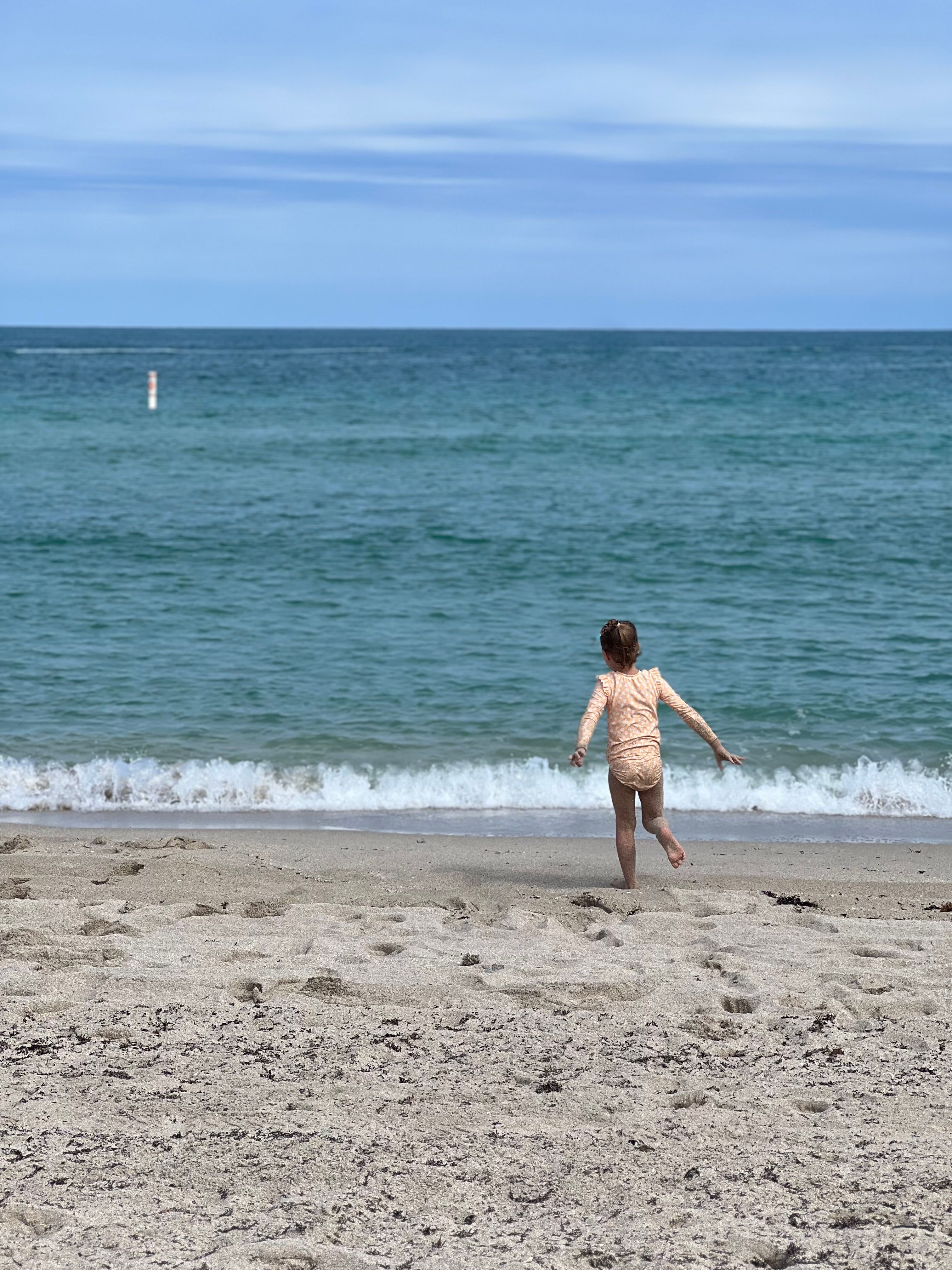A young girl runs towards the ocean waves at Bal Harbour Beach, FL.