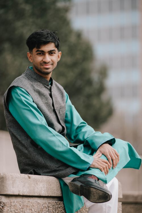 Free Portrait of a young man in traditional Indian attire sitting on a park bench with a smile. Stock Photo