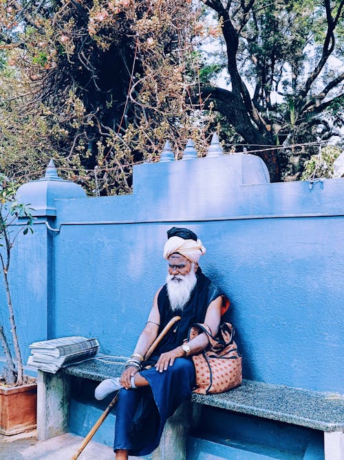 An old man sitting on a bench in front of a blue wall