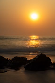 Peaceful sunset over an ocean with silhouetted rocks, golden reflections, and tranquil waves.