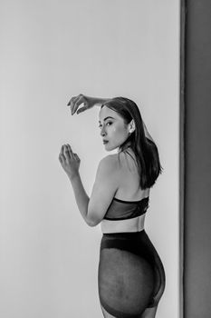 Black and white portrait of a model in lingerie with arms raised, studio setting.