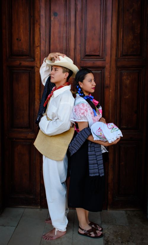 Free A young couple in traditional clothing pose back to back in front of a wooden door. Stock Photo