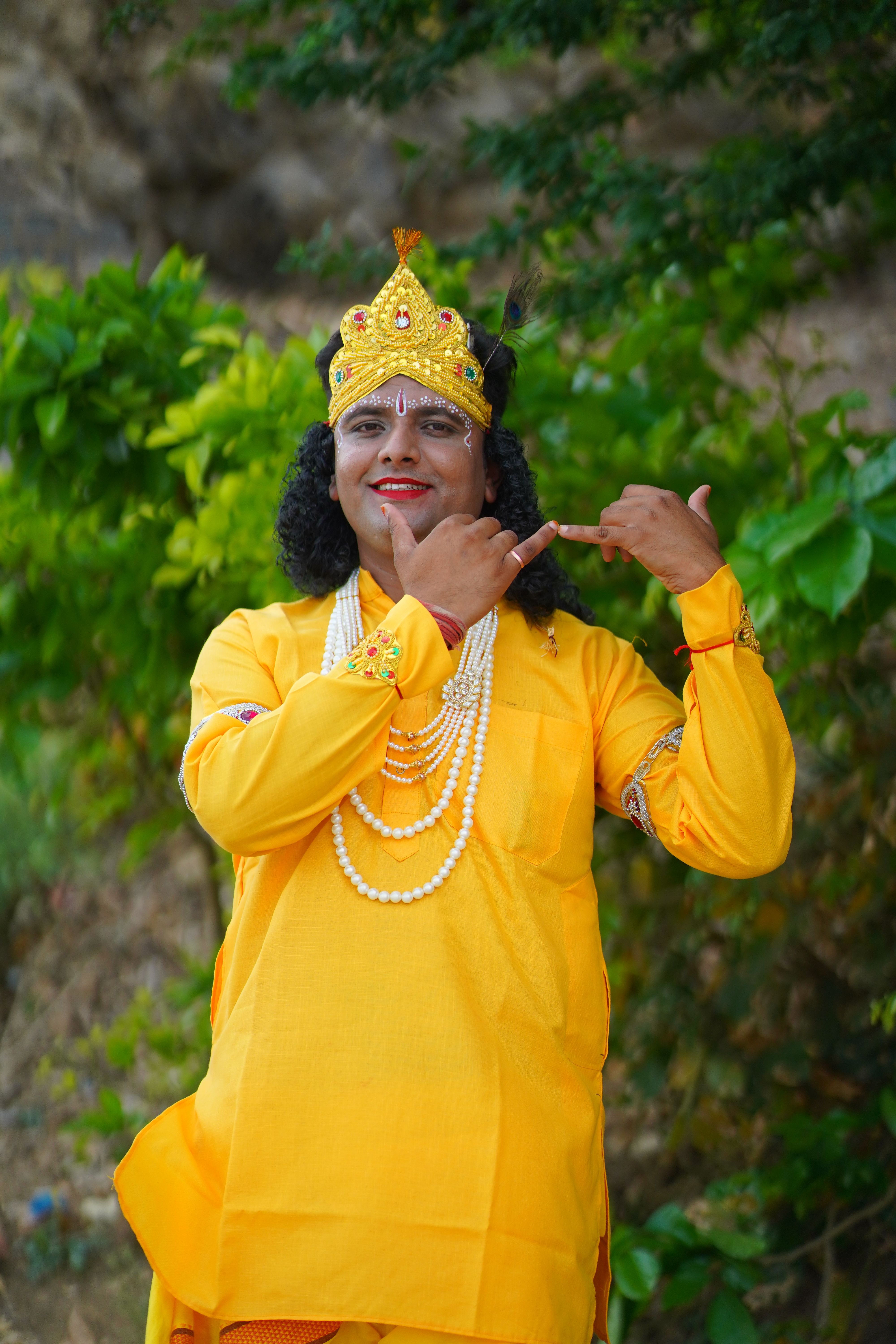 Man in Hindu deity attire performing outdoors, wearing traditional jewelry and kurta.