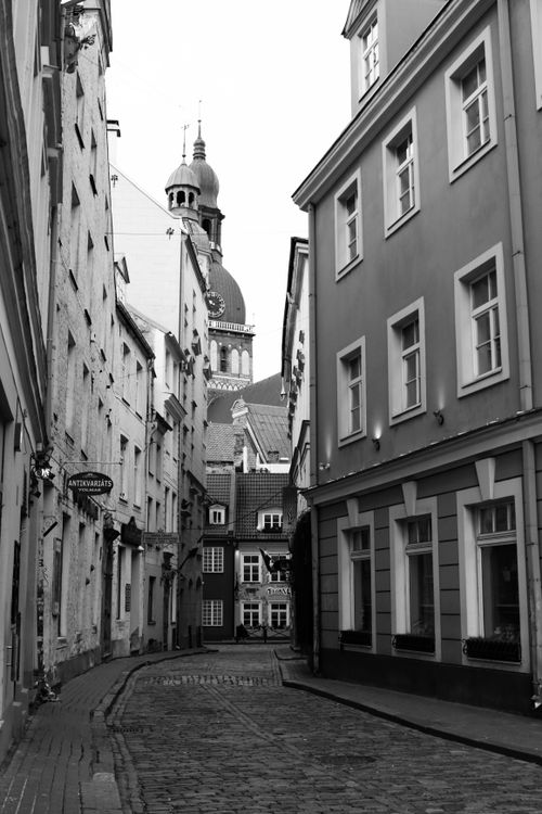 Free Black and white photo of a narrow cobblestone alley in Riga's Old Town, showcasing historical architecture. Stock Photo