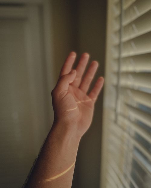 Free A human hand reaches towards light filtering through window blinds, creating an abstract play of shadows. Stock Photo