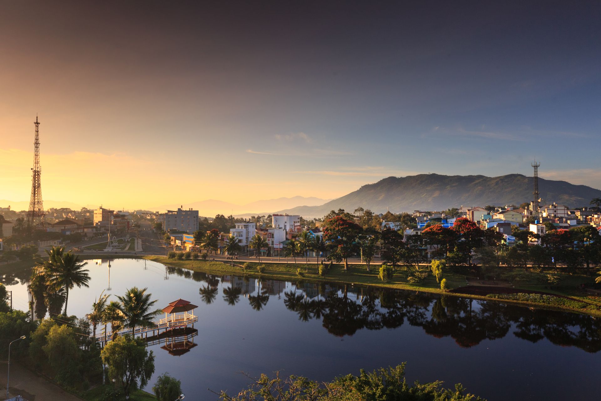 Peaceful cityscape at sunrise with reflections in a tranquil lake and mountains in the background.