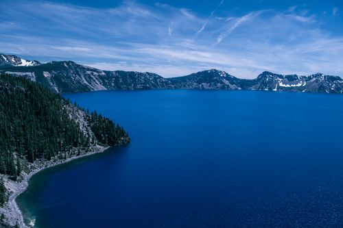 Free A breathtaking aerial view of Crater Lake surrounded by forested mountains under a clear blue sky. Stock Photo