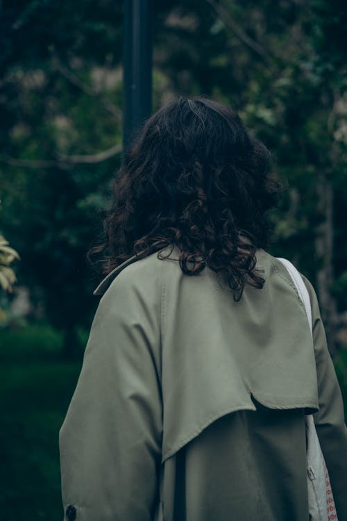 A woman in a green trench coat is walking down a sidewalk