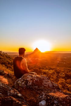 一个人坐在岩石上，凝视着山峰间如画的日出，四周环绕着大自然