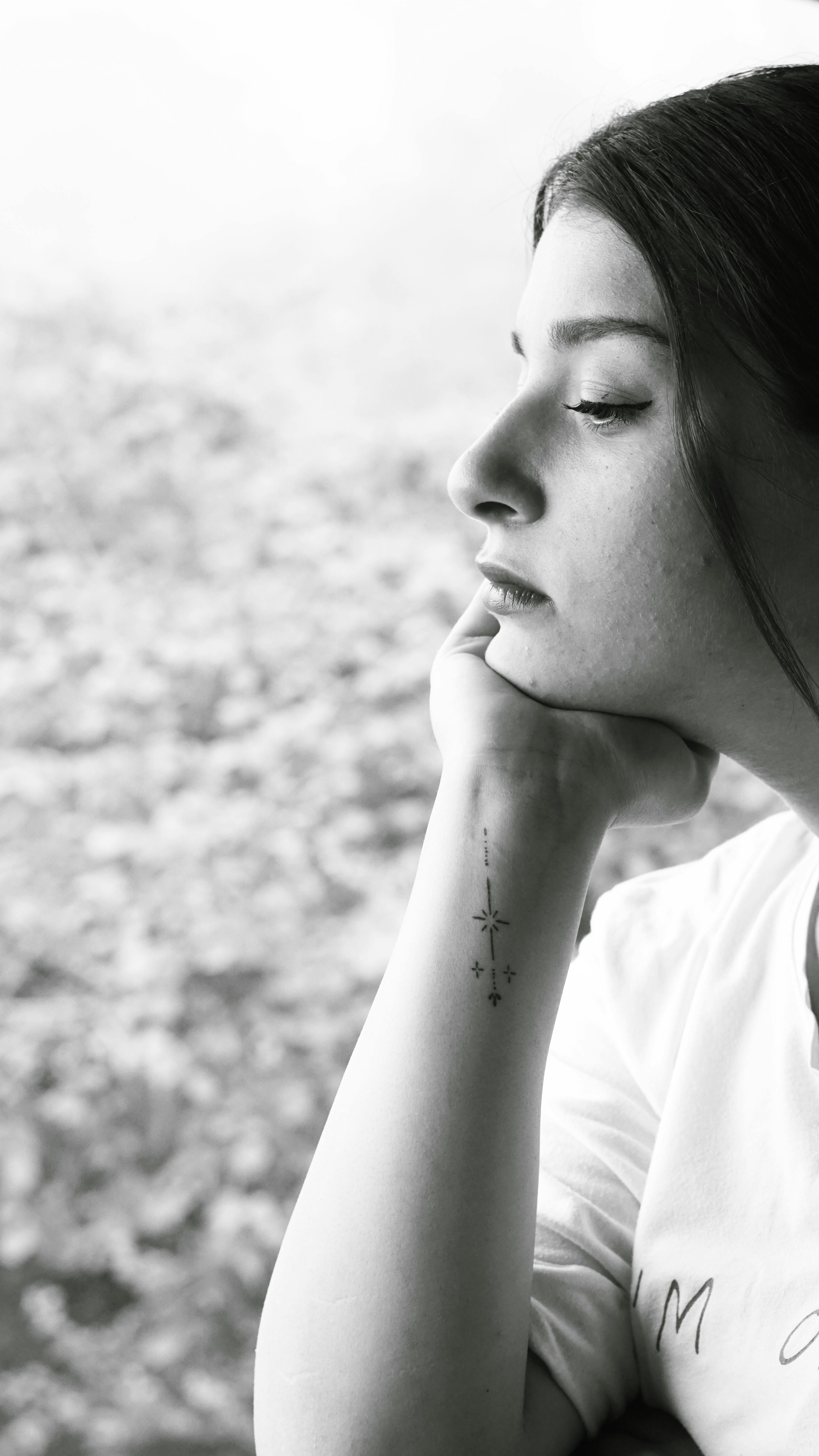 Black and white portrait of a woman in profile with a tattoo, exuding introspection.