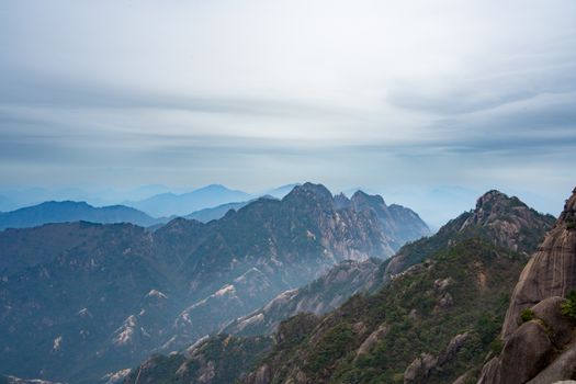 A breathtaking view of mist-covered mountains layered under a cloudy sky.