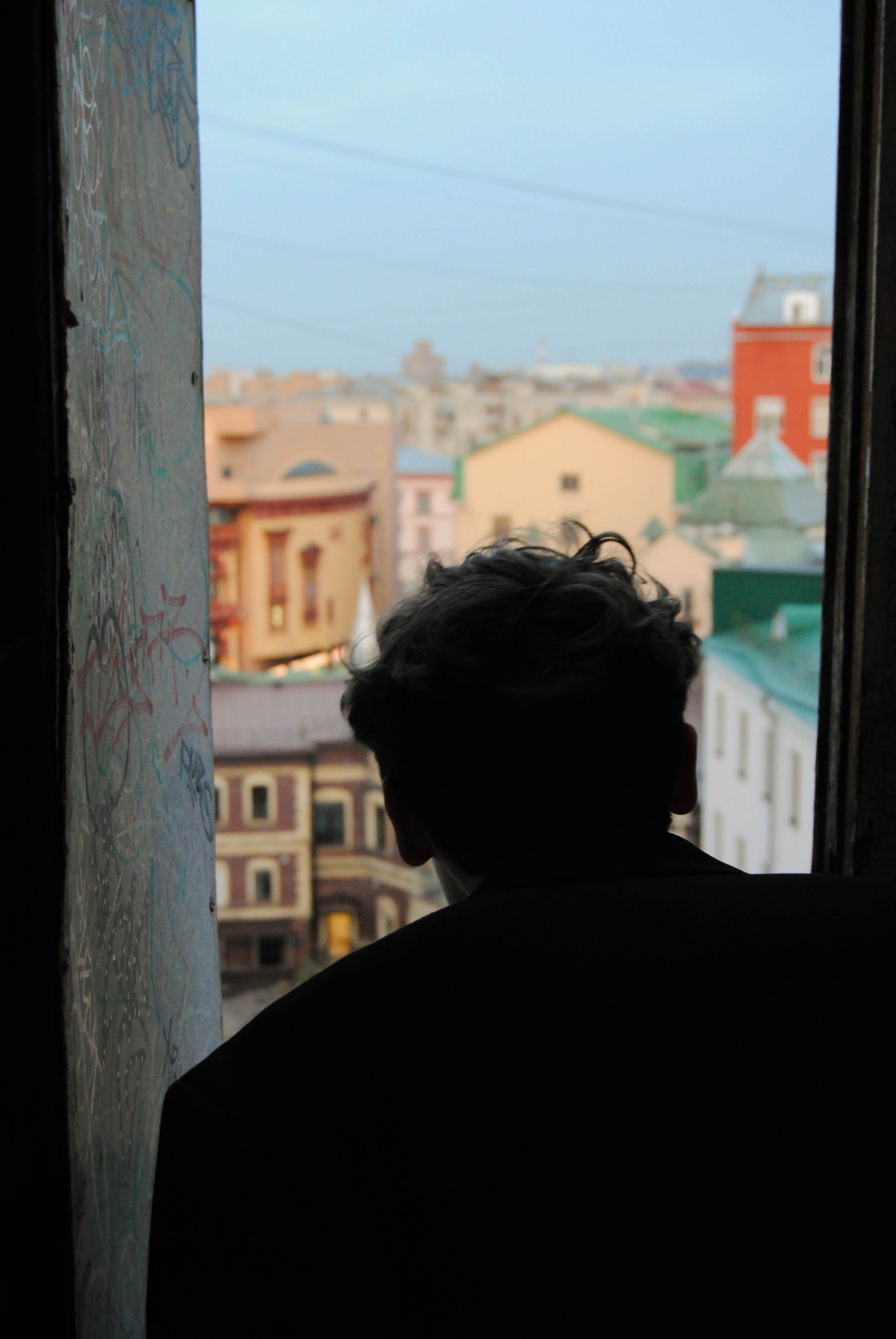 Silhouette of an adult looking out a window over Moscow's urban skyline.